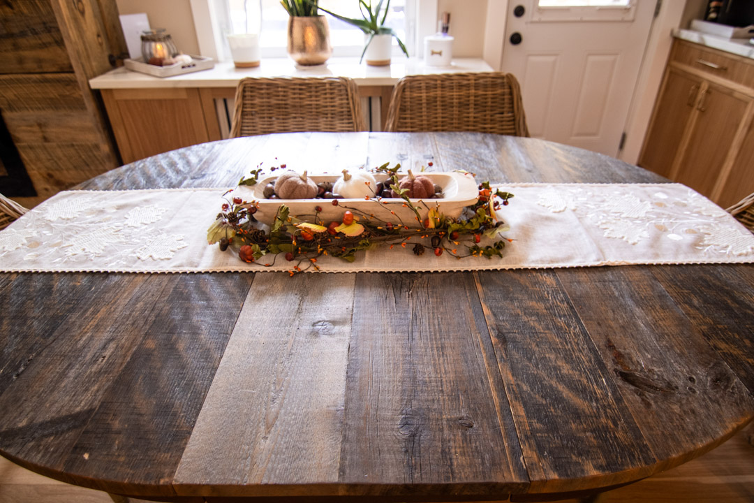 Close-up of custom dining room table top with white runner and harvest themed centerpiece.