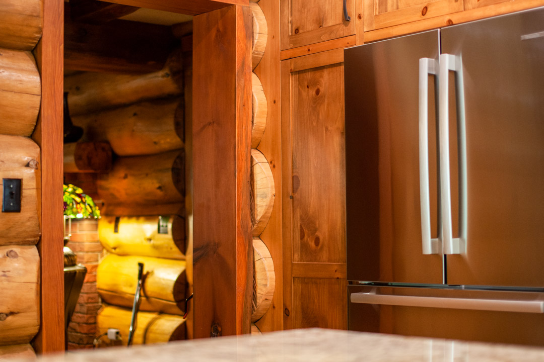 Wooden cabinetry around stainless steel fridge in log home.