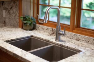 Two deep sunken kitchen sinks with stone counters and stainless steel faucet.