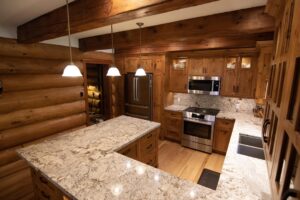 Large custom kitchen in natural wood with stone counters and breakfast bar with pendant lighting above.