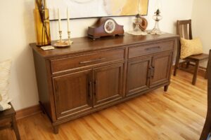 Restoration of antique wooden buffet in dining room with two dining room chairs on either side.