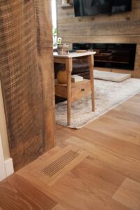 View of wooden side table beside a couch, with custom wood vent cover in floor.