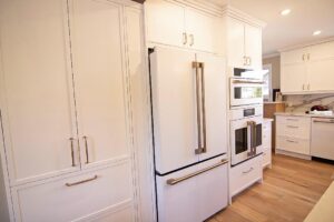White custom cabinetry surrounding a white fridge with double doors, and built-in oven and a microwave.