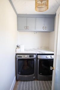 Light blue grey custom cabinetry with marble counter top in a laundry room.